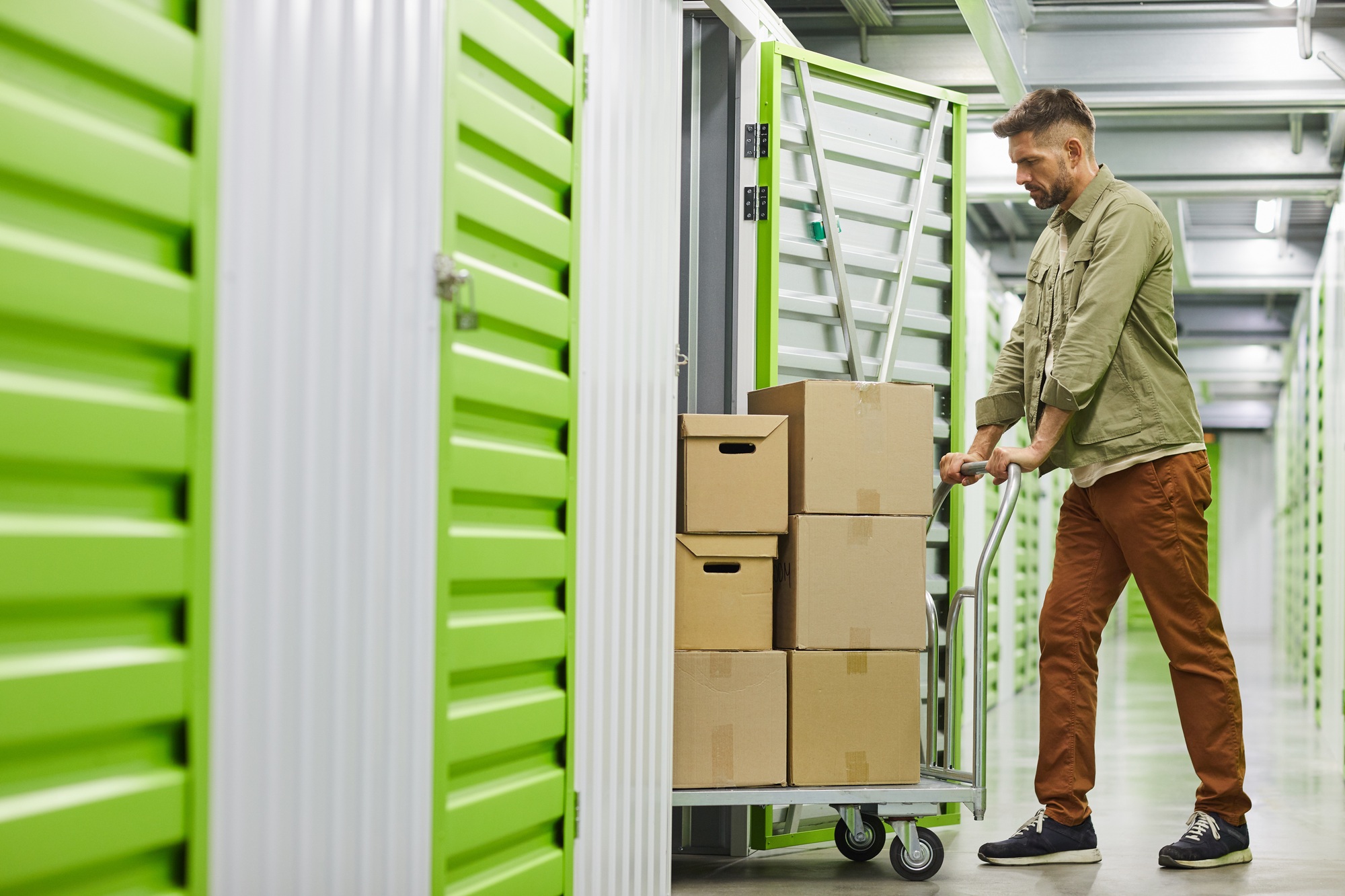 Homme poussant un chariot avec des cartons dans une zone de stockage verte, illustration de préparation et logistique pour bien préparer son déménagement fiche pratique