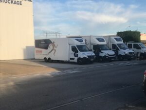 Flottes de camions de déménagement blancs garés le long d’un trottoir près d’un bâtiment.